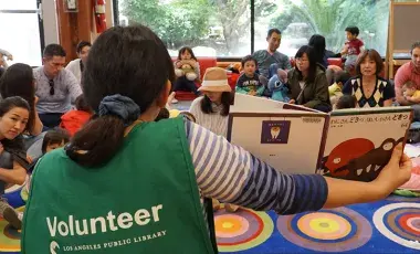 Person in green "volunteer" vest holding book up to audience