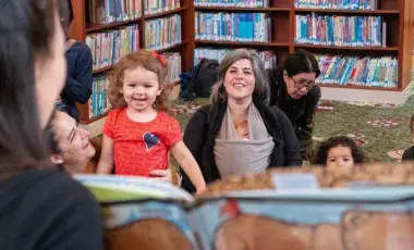 Babies and toddlers looking at a reader holding up a book