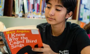 Teen girl holding up a book and reading.