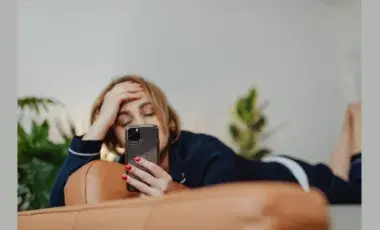 young person laying on a couch with a smartphone obscuring their face