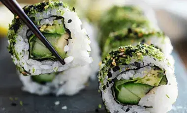 a plate of vegan sushi with one sushi grasped by black chopsticks