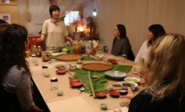 People seated at a table watching a woman do a demonstration