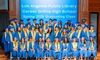 cohort of graduates pose in caps and gowns
