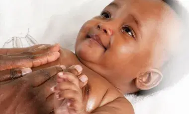 a baby looks up as adult hands massage the baby