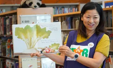 STAR volunteer holding up a picture book to read to an audience