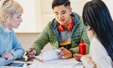 Teens collaborate at a table over papers