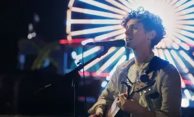 Person singing at a microphone in front of a lit-up ferris wheel.