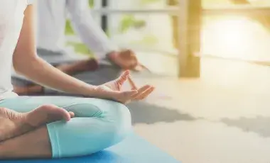 Two people seated on a floor in a yoga position with sunlight shining on them from the side.