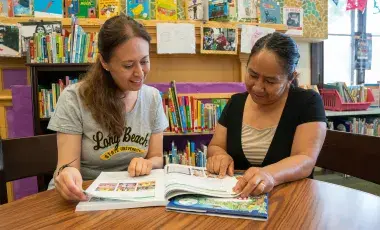 A tutor and adult learner are looking through a workbook.