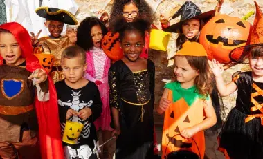 Children wearing Halloween costumes standing together with trick or treat bags