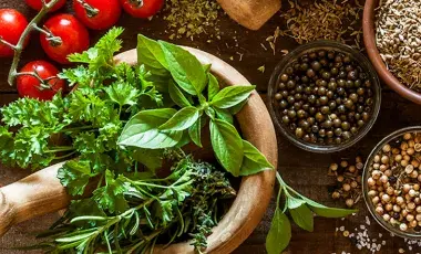 Fresh herbs rest in a mortar beside tomatoes and spices