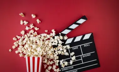 Over-flowing popcorn box next to a film clapper.