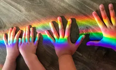 Hands with a rainbow shining across them.