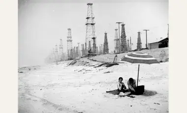 A couple spread out a picnic in the shadows of Huntington Beach oil derricks, circa 1937