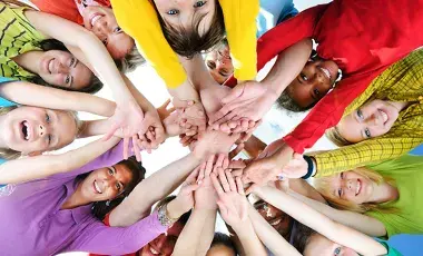 A diverse group of smiling people put their hands together in a circle