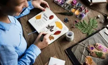 Person creating a nature journal with leaves and flowers.