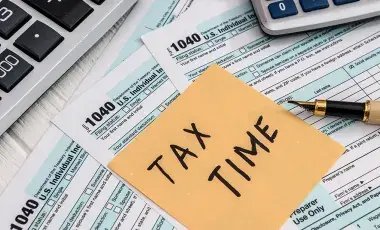  tax time written on a post-it note with tax paperwork, a pen and calculator in the background