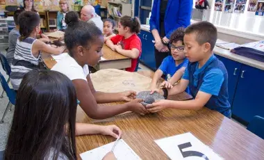 children place hands on a historical object in a classroom. 