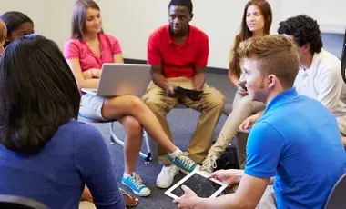 Teens sitting in a circle holding a laptop and an iPad.
