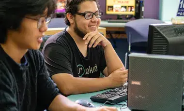 Two boys smiling and using desktop computers