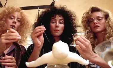 The three witches, Susan Sarandon, Cher, and Michelle Pfeiffer are pocking a voodoo doll with needless