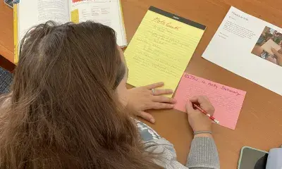 person writes at desk with various materials