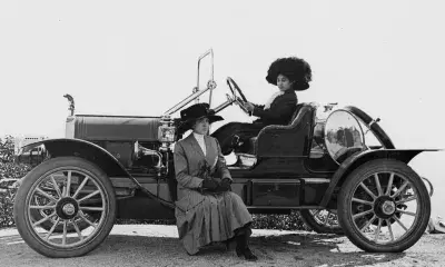 Women Drove Automobile Innovation, circa 1910, features two women, one sitting in the driver's seat, the other sitting on a ledge on the outside of the car.