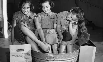 Three Girl Scouts sit with feet in basin, 1960