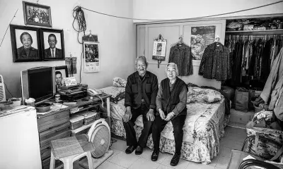 Two people sit on bed in bedroom