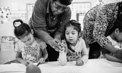 Older adult hovers over two young children sitting at table