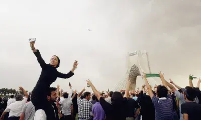 Crowd of people at festival with person on top of someone's shoulders taking selfie