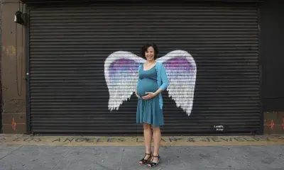 portrait of person holding pregnant belly in front of wings