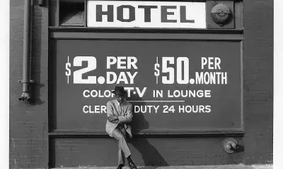 person leans against exterior wall that reads "Hotel, $2 per day. $50 per month"