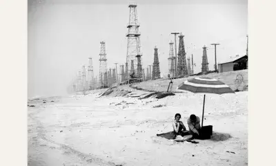 A couple spread out a picnic in the shadows of Huntington Beach oil derricks, circa 1937