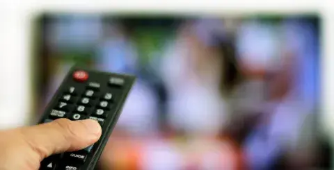 hand holding a remote with a tv screen in the background