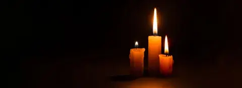 Three burning taper candles against a black background.