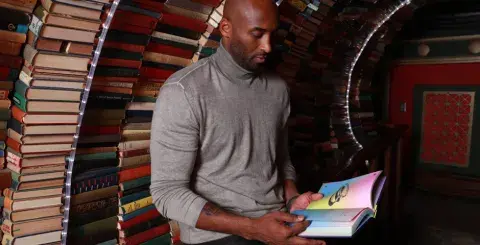 Kobe Bryant reads a book with The Last Bookstore's book tunnel in the background
