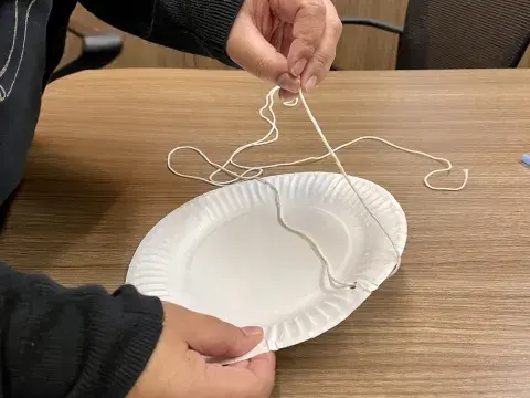 person threads string through hole in plate