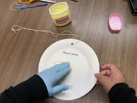 person wearing latex gloves rubs petroleum jelly onto paper plate