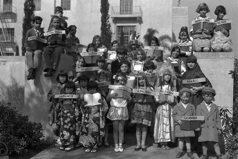 Children dressed in various costumes holding signs with various languages.