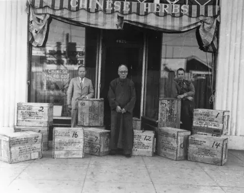 Three men standing outside a Chinese Herbs shop.