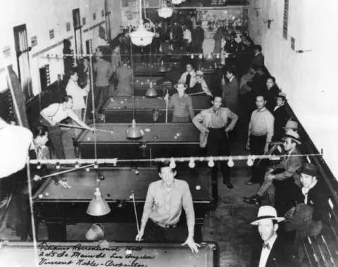 A recreation hall with men playing at pool tables.
