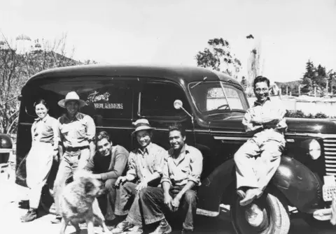 Six employees and a dog in front of a flower delivery truck.