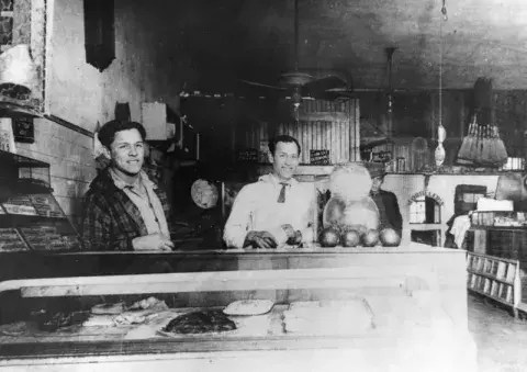 Two people standing behind the counter of a grocery store.