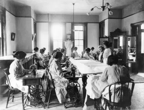 Students seated at a knitting machine.