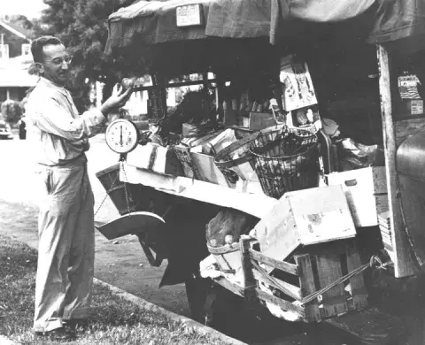 A person inspecting an apple with one hand near a produce truck.
