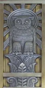Owl metalwork on a door. The owl is perched on top of a column with a halo behind its head.