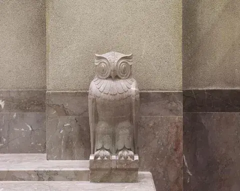 A stone owl on the exterior steps of a building.