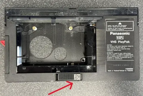 Panasonic VHS-c adapter with an arrow at the bottom pointing at the door lever.