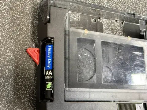 Panasonic VHS-c adapter battery slot with AA battery inside with a red triangle behind it.